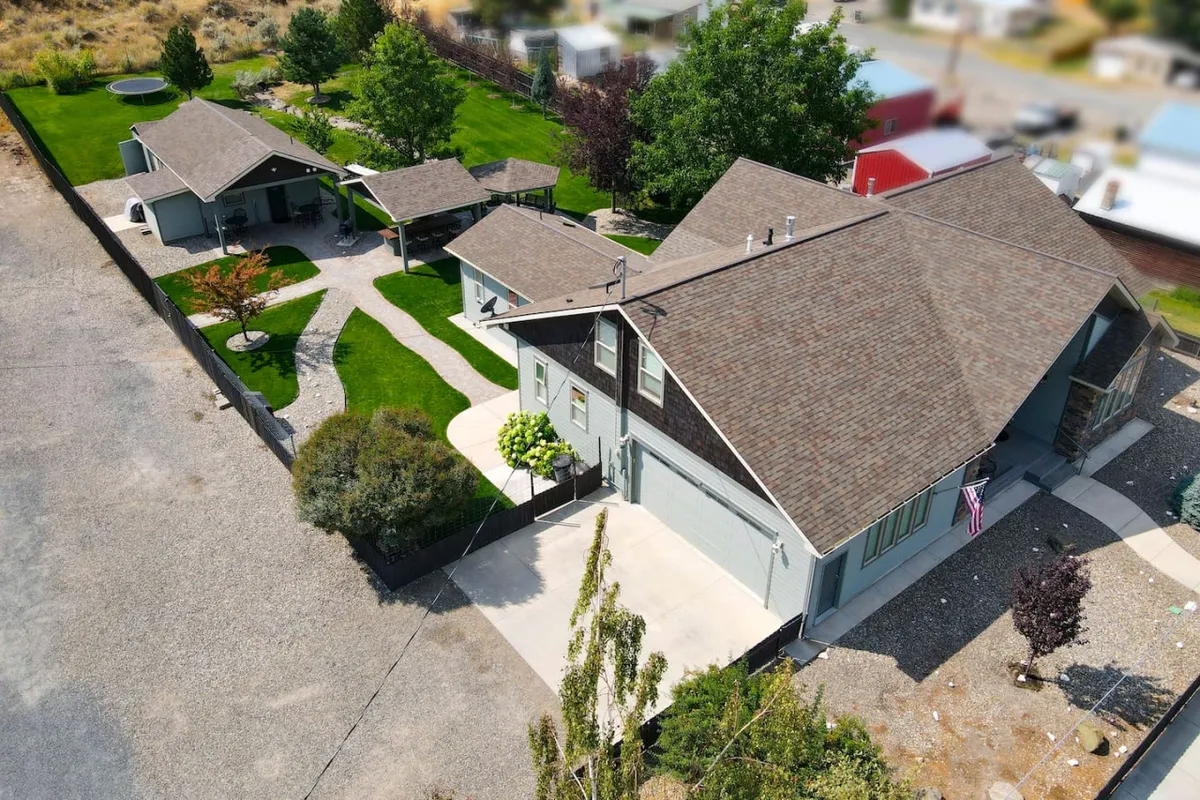 A wide view of the main house’s outdoor seating area surrounded by a landscaped garden. The patio is set for family gatherings, outdoor dining, and moments of relaxation, with lush greenery and open space inviting wellness breaks.