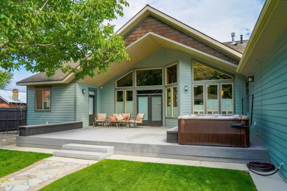 This image captures a welcoming deck area featuring a spacious hot tub, comfortable outdoor seating, and large windows that connect to the home’s interior. The setting exudes a casual, inviting atmosphere perfect for both relaxation and entertaining guests outdoors.