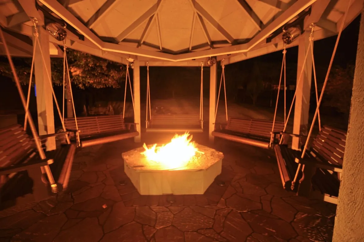 A cozy fire pit area with swing seats under a ceiling structure, designed for gathering and storytelling. The inviting setup encourages evenings spent sharing stories and stargazing in a warm, communal outdoor space.