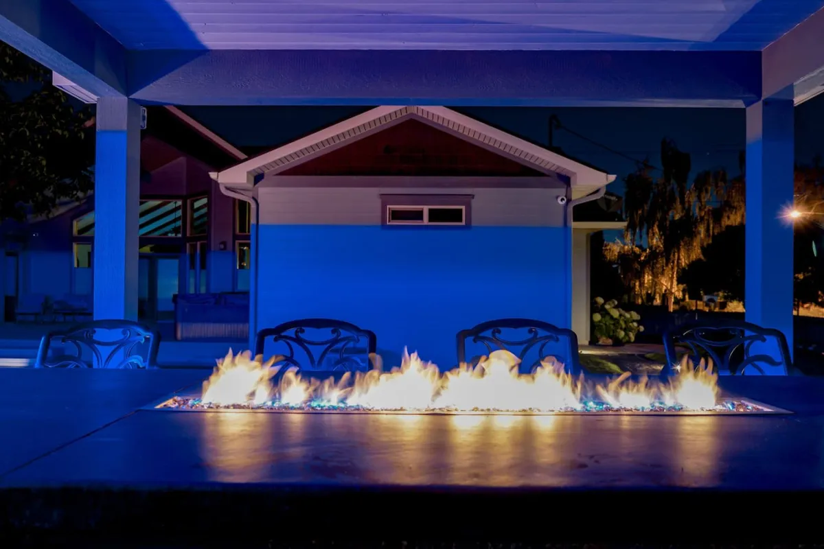 This nighttime scene centers on a glowing fire pit surrounded by ample outdoor seating. The arrangement is designed for group gatherings, with the fire providing a cozy focal point. The backdrop includes the night sky, enhancing the sense of relaxation and community under the stars.