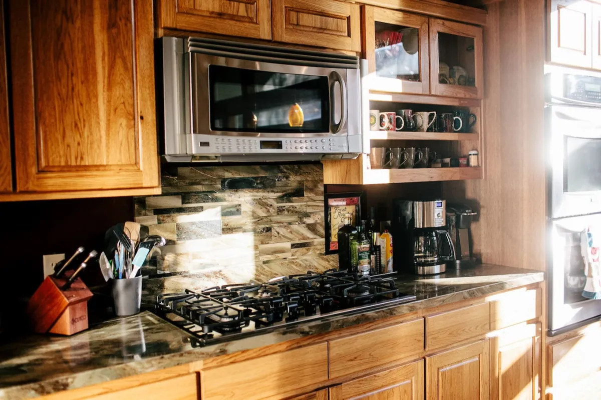 A close-up view of the kitchen’s cooking area reveals a stainless steel microwave, a prominent gas stove, wooden cabinets, and a selection of kitchen utensils ready for use. The layout is inviting and practical, suggesting this is a well-equipped space for cooking elaborate meals or casual fare alike.