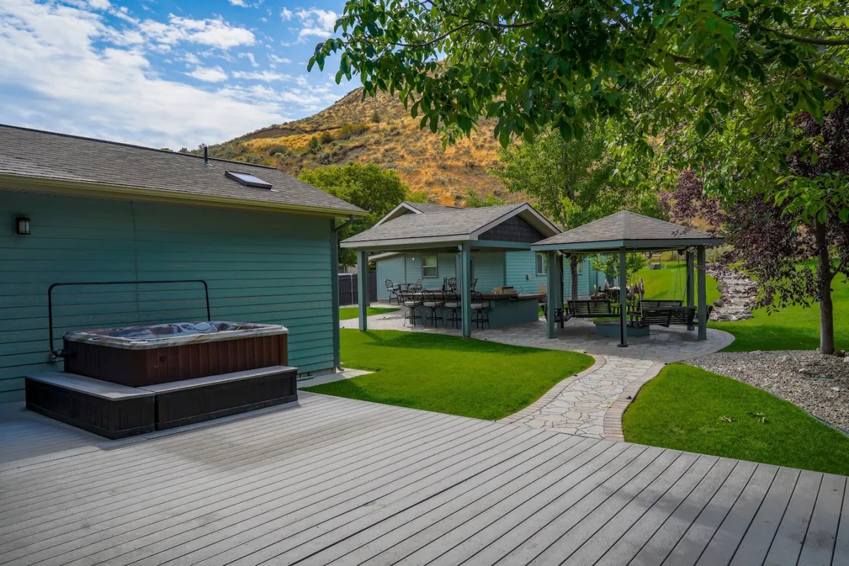 This image highlights a tranquil outdoor setting featuring a hot tub, outdoor dining area, landscaped pathways, and lush greenery. The atmosphere is serene and welcoming, showcasing inviting spaces for relaxation and group gatherings after a day of golfing.