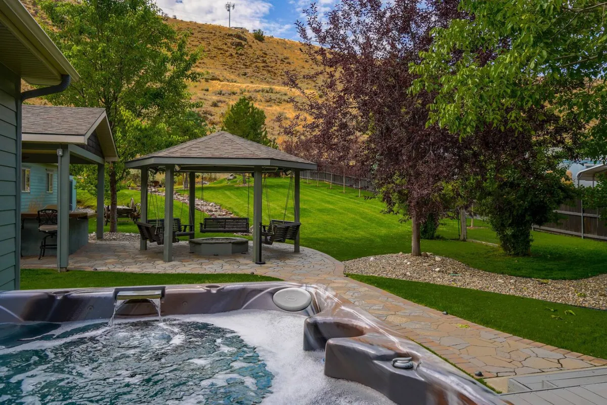 An inviting exterior scene featuring a hot tub nestled beside a green lawn and a gazebo. The stone pathway and surrounding greenery create a tranquil environment perfect for relaxation after a day on the slopes.