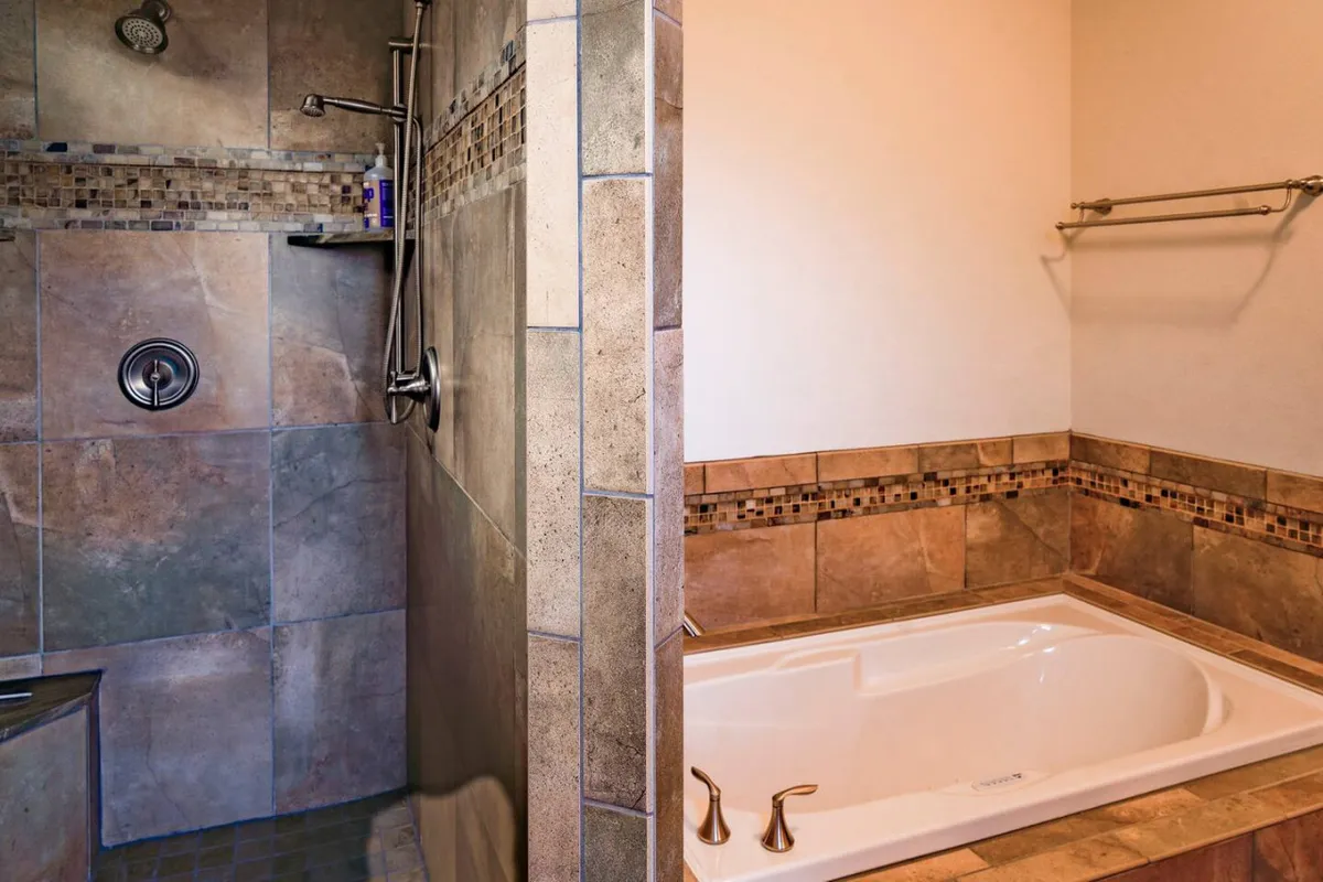A tranquil bathroom showcasing a large bathtub, a separate shower area, and stylish decorative tile accents. The space is designed for indulgence and relaxation, evoking a spa-like experience.