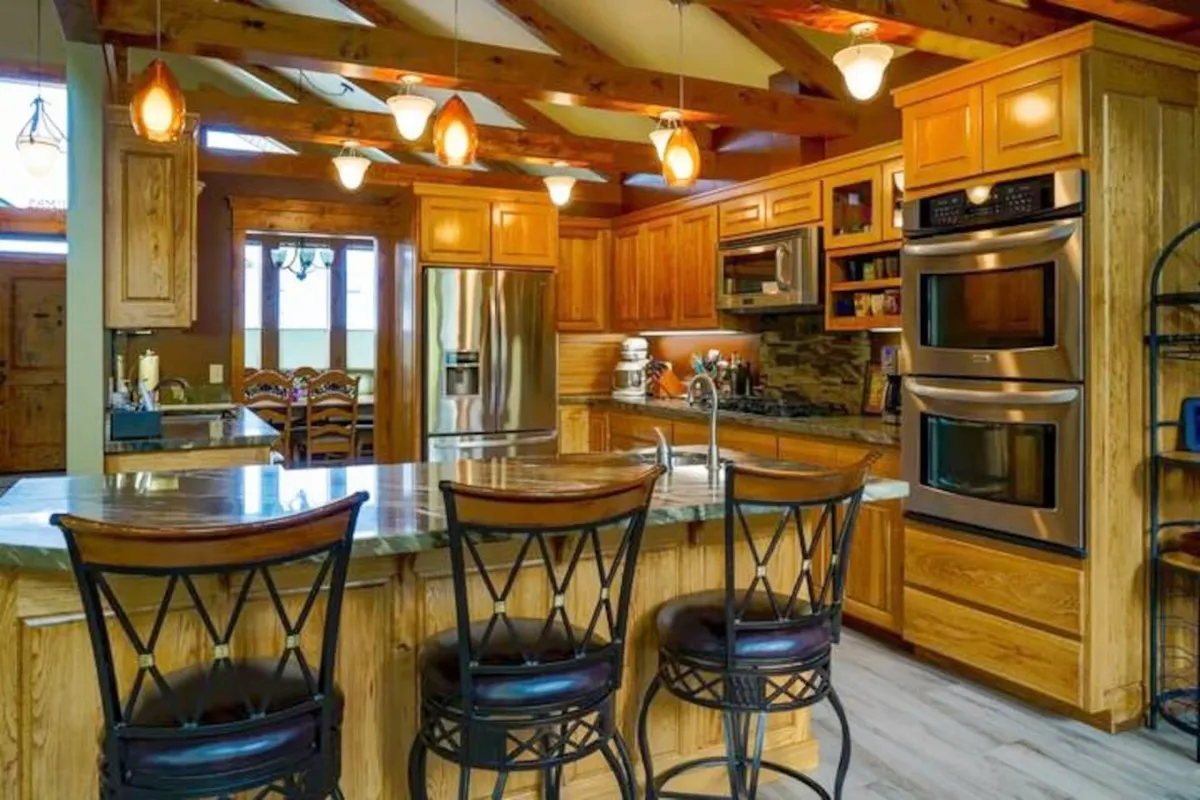 This image features the kitchen’s island seating, a well-organized appliance layout, and warm wood cabinetry. The setting is clearly designed for both cooking and socializing, with ample space for multiple people to participate in meal prep or simply gather around. The overall ambiance is warm and welcoming, ideal for group cooking sessions.